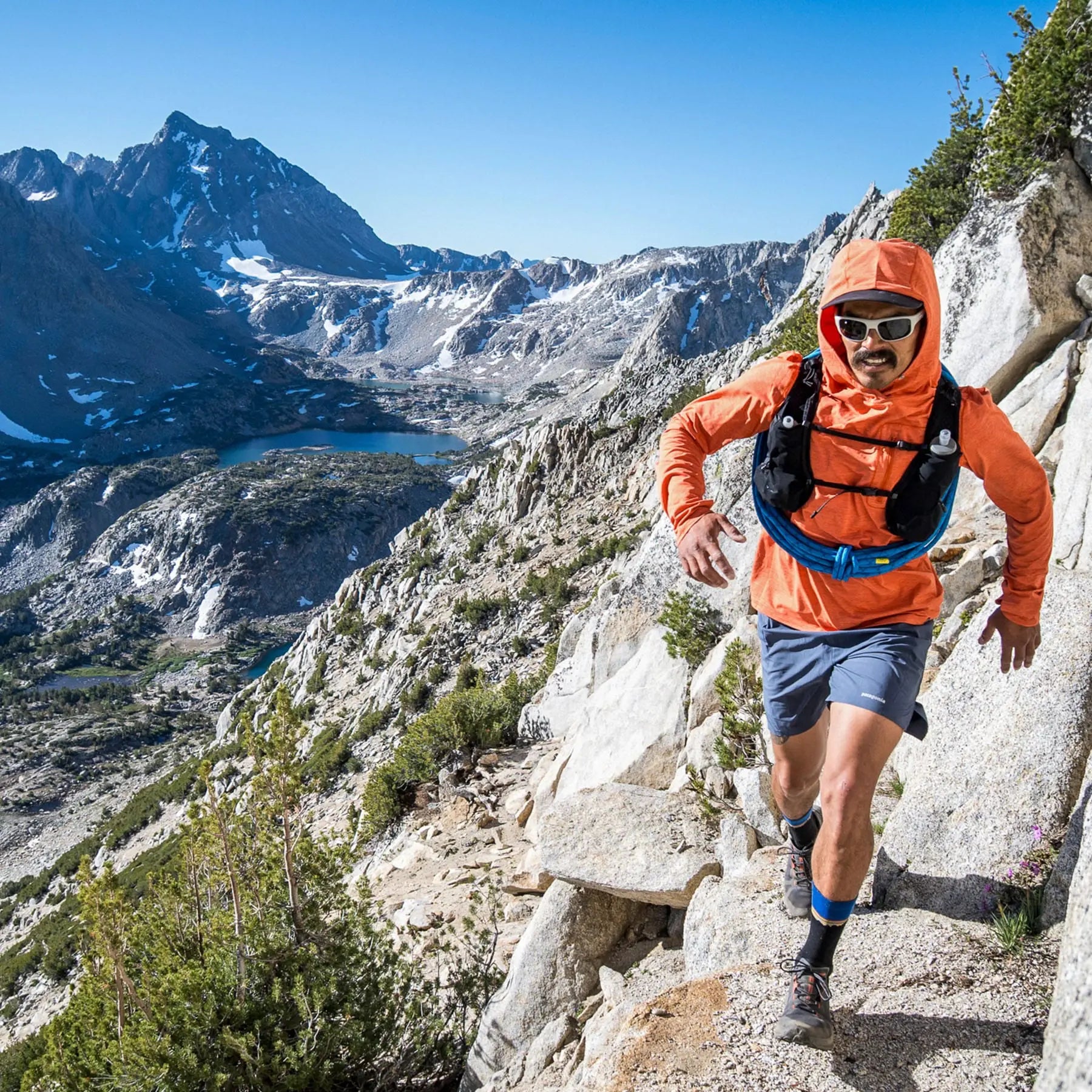 Man hiking on a mountain trail with a scenic view of mountains and lakes in the background.