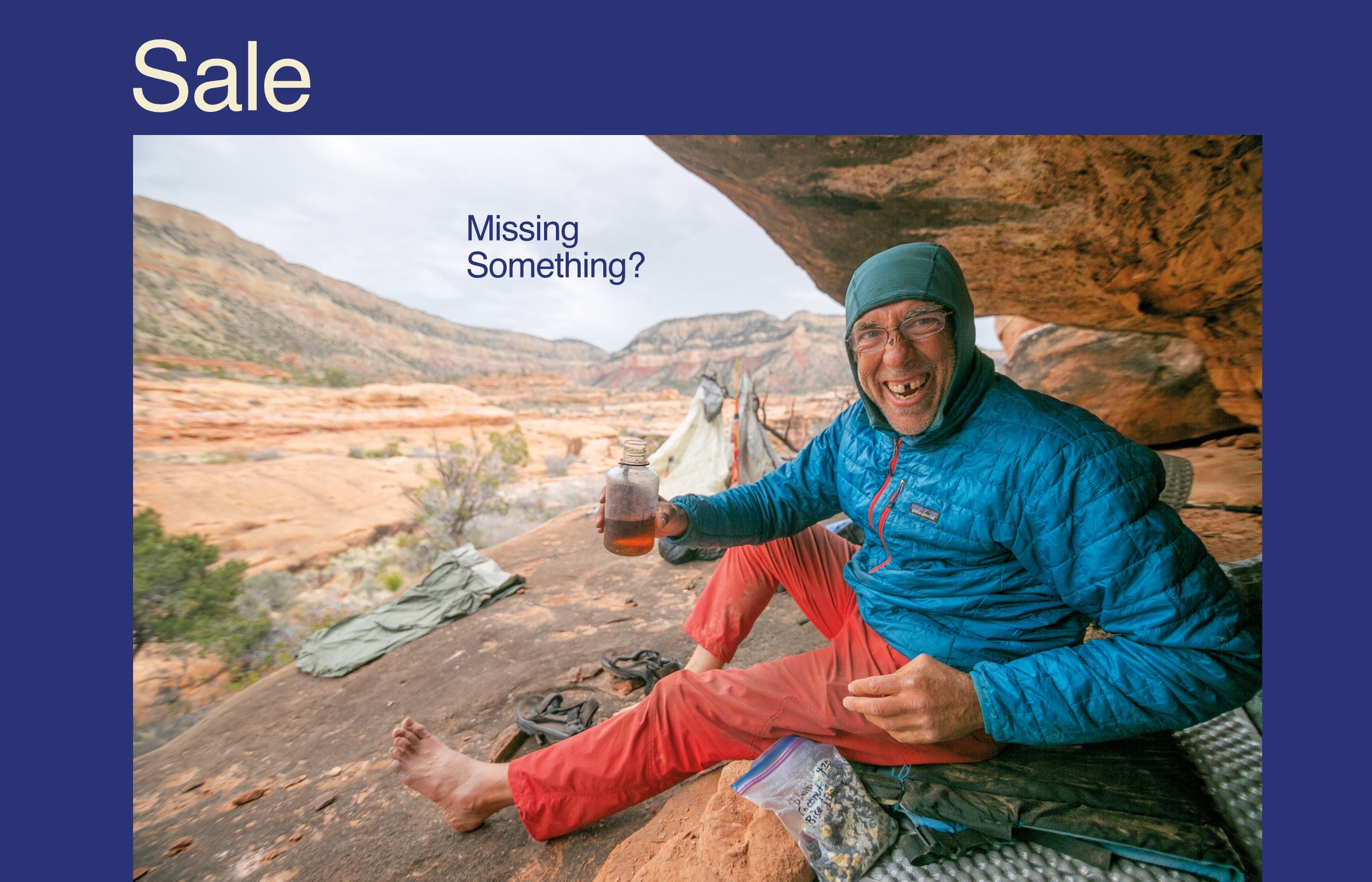 A lifestyle promotional image featuring a smiling man in a blue puffer jacket and red pants sitting in a rocky desert canyon, holding a glass of beer. The image has a dark blue border with the word 'Sale' in white at the top left and 'Missing Something?' text overlaid near the top center.