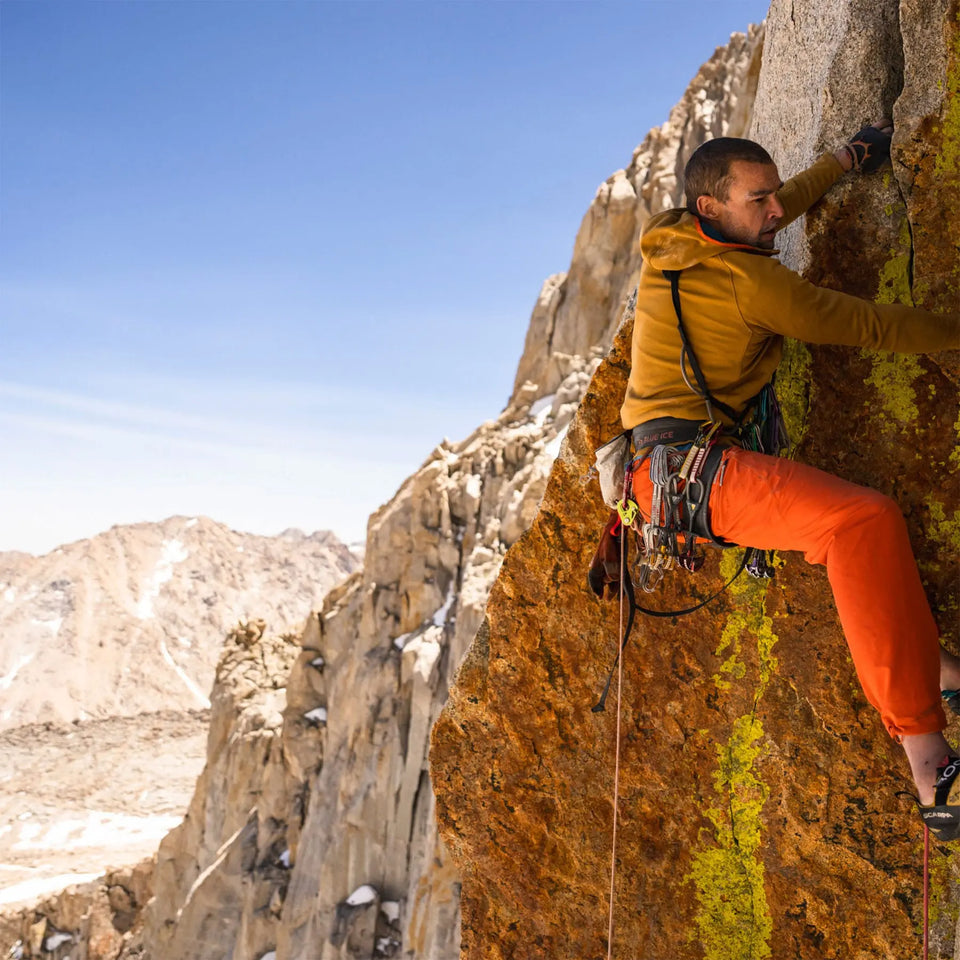 Climber in a brown fleece and orange pants scaling a rock face.