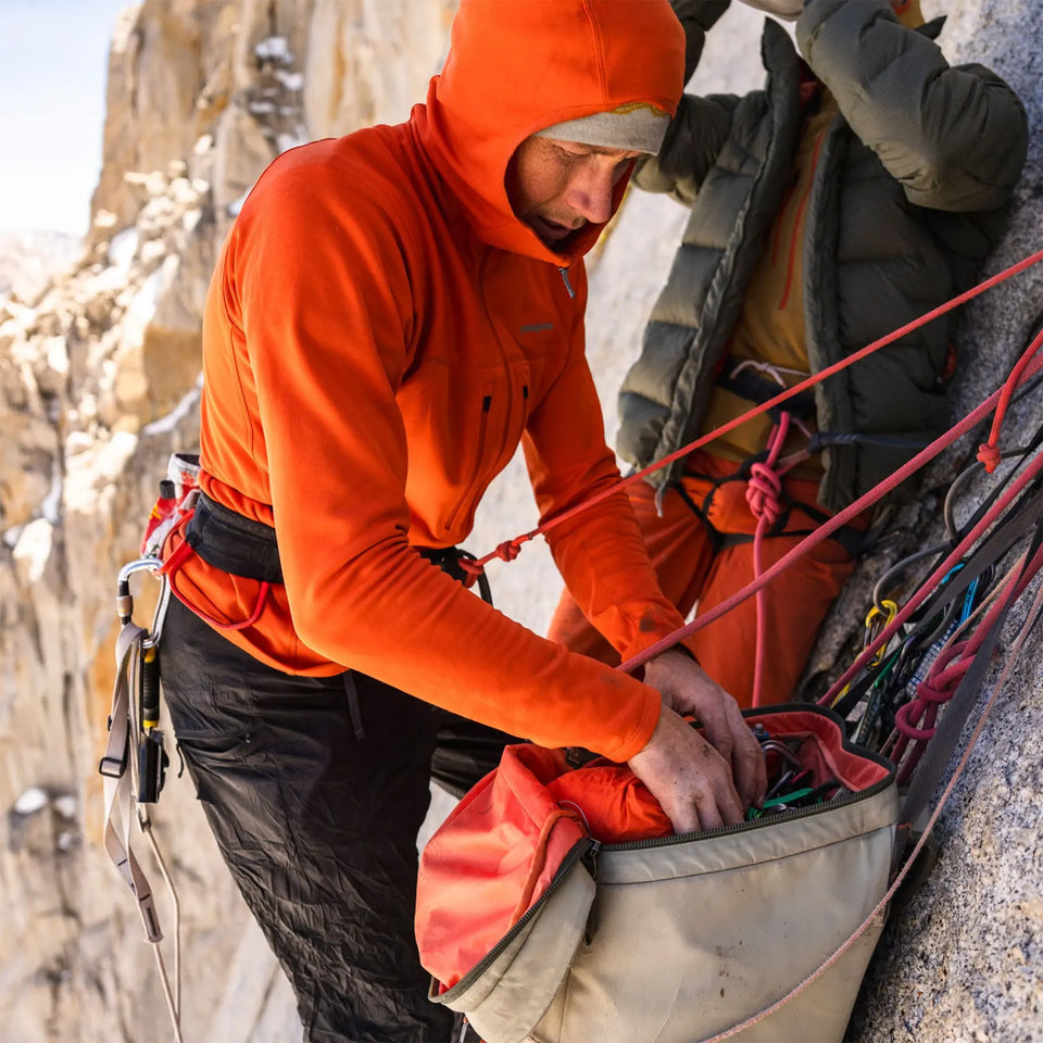Person in orange jacket preparing climbing equipment on a rocky mountain