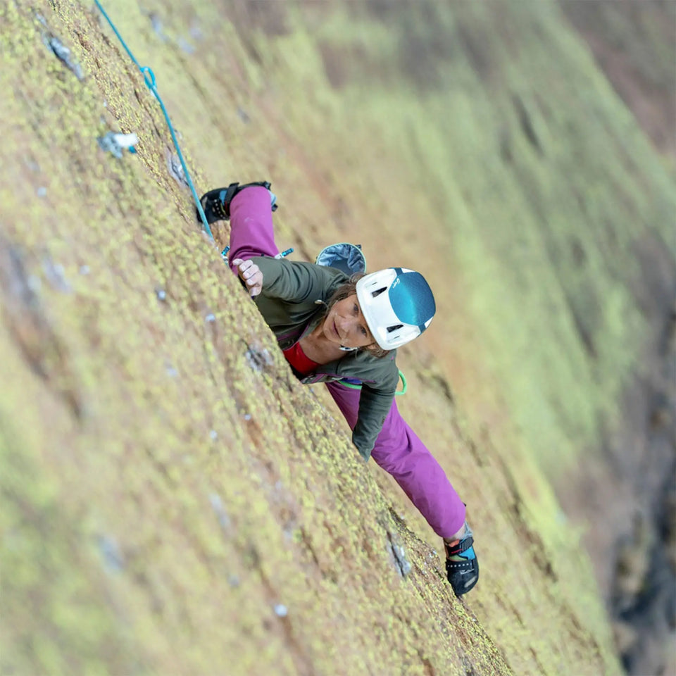 Person climbing a steep rock face wearing a helmet and climbing gear.
