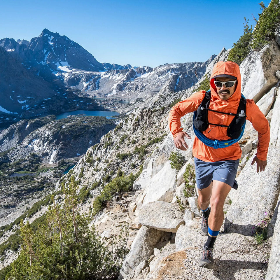 Man hiking on a mountain trail with a scenic view of mountains and lakes in the background.