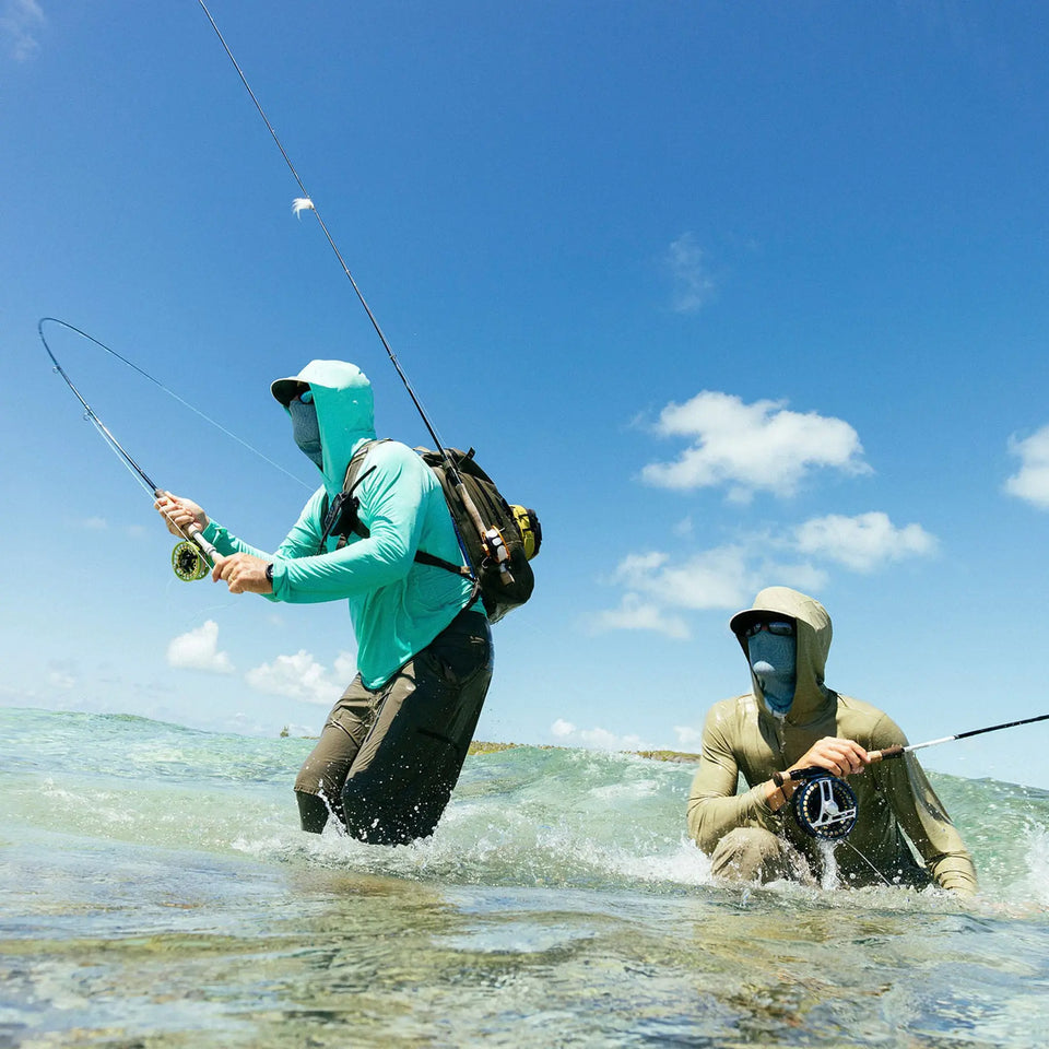 Two anglers thigh deep in clear water casting their fishing rods.