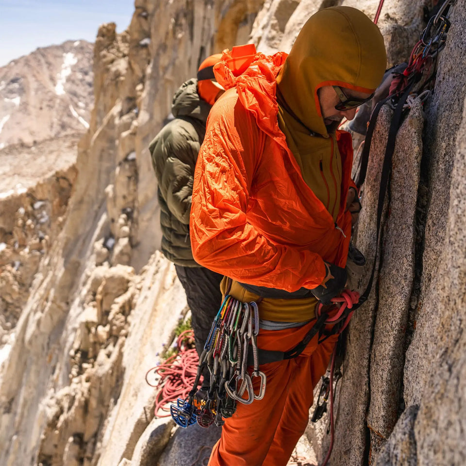 Person in orange climbing gear scaling a rocky mountain face.