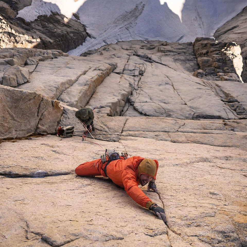 Man in a orange jacket climbing up a granite cliff face.