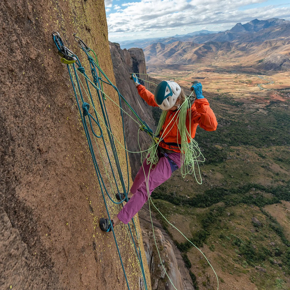 Person rock climbing on a steep cliff with a scenic mountain landscape in the background