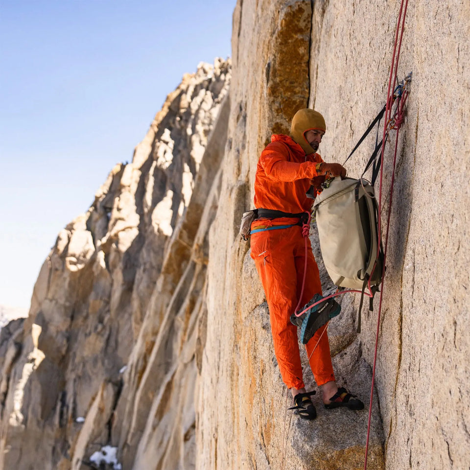 Person in orange climbing gear scaling a rocky cliff face.