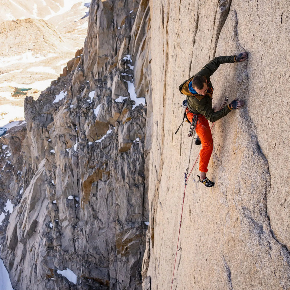Person climbing a steep rock face with ropes and climbing gear.