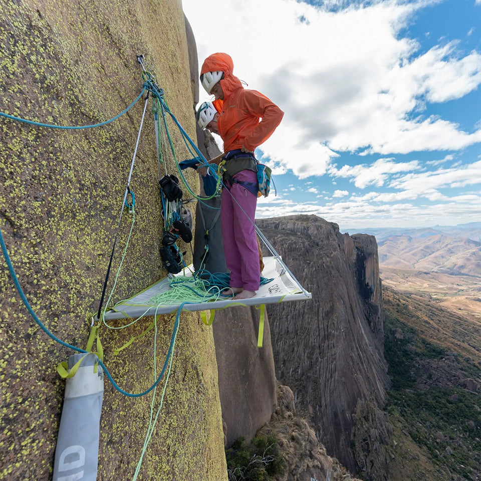 Person on a portaledge attached to a rock face with a scenic background