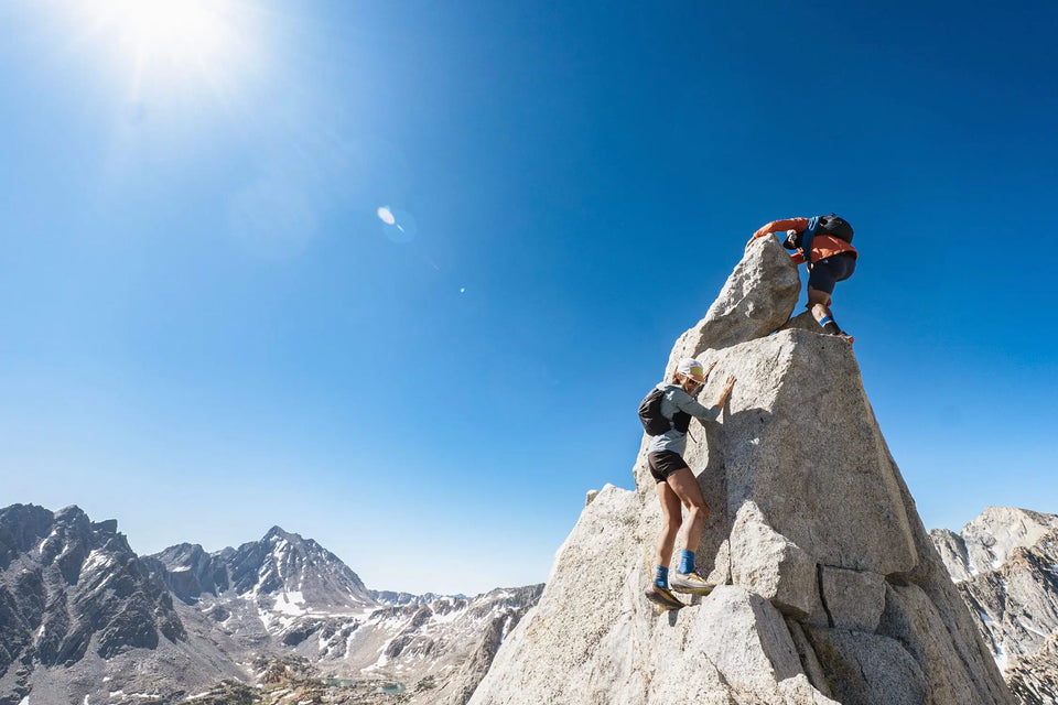 Two climbers on a rocky mountain peak with a clear blue sky