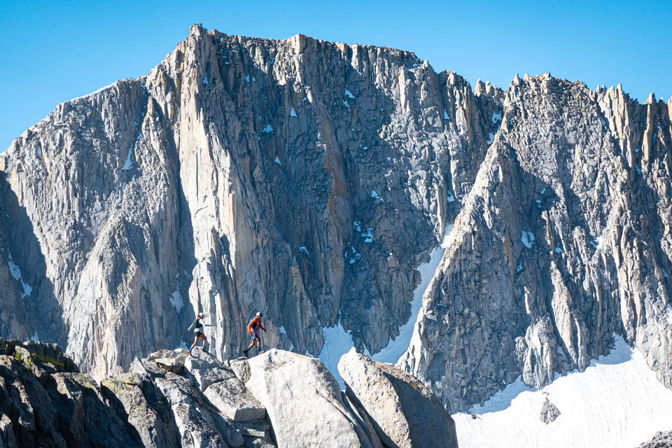 Two climbers on a rocky outcrop with a large mountain peak in the background